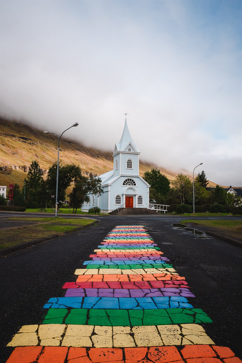 A colorful rainbow path guides the way to Seyðisfjörður’s iconic white church in the heart of Iceland’s quirkiest fjord town.