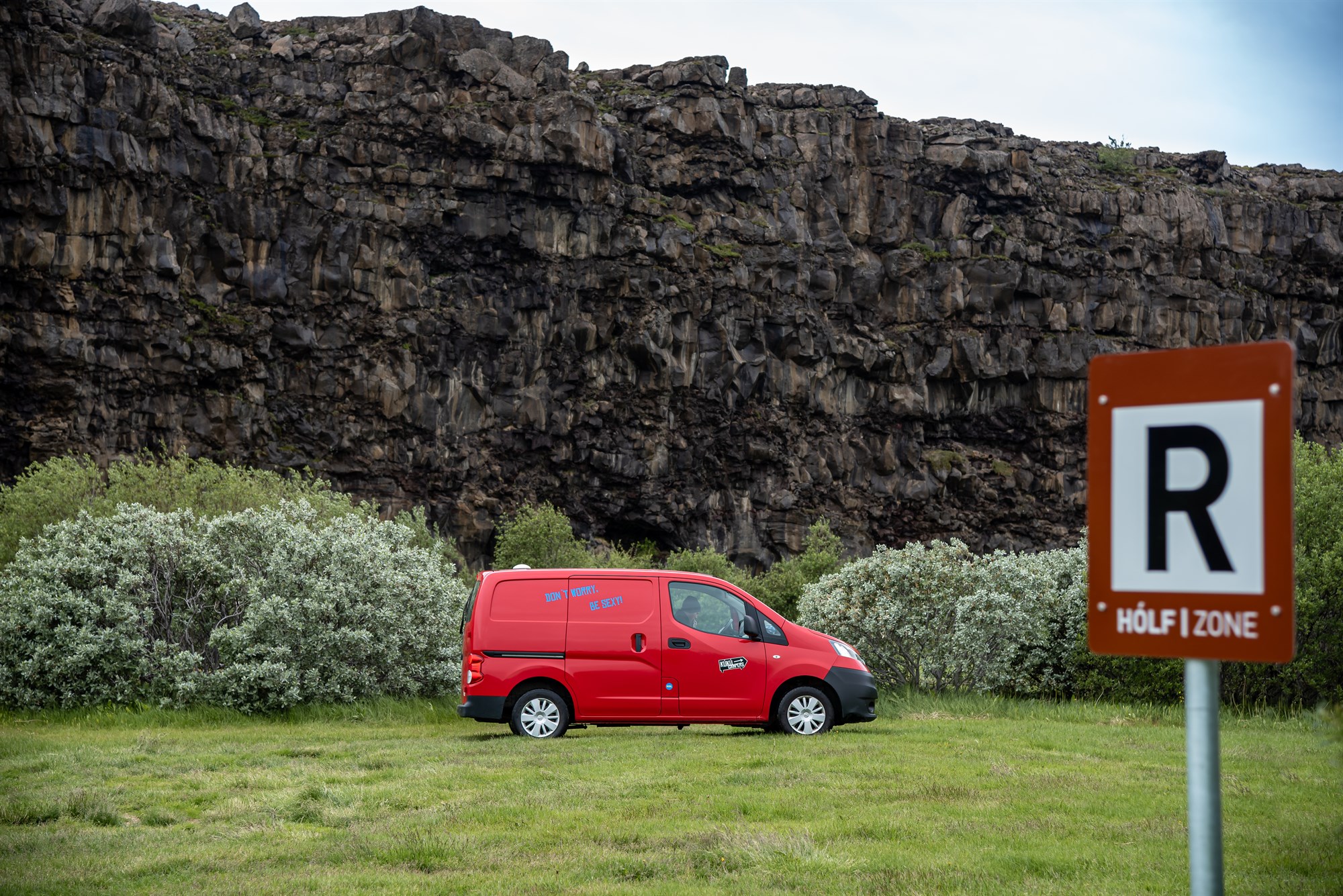 A bright red camper van parked at the base of Ásbyrgi’s towering canyon wall, next to a “Hólf Zone” sign – camping with serious Norse energy.