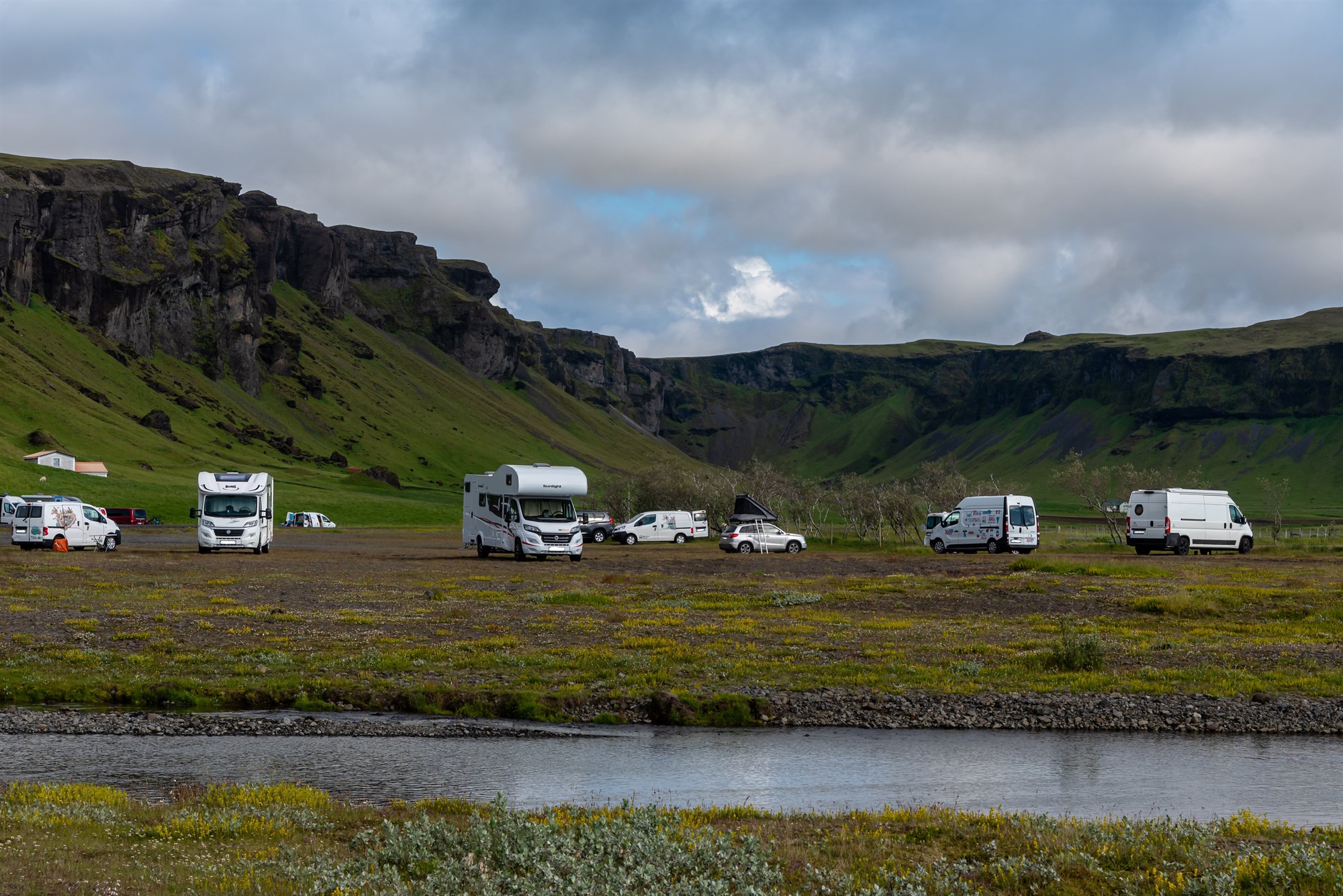 Hidden Gem Vibes at Kleifar Campsite A quiet campsite scene with several camper vans parked beneath rocky cliffs, wrapped in greenery and Icelandic stillness just off the beaten path.