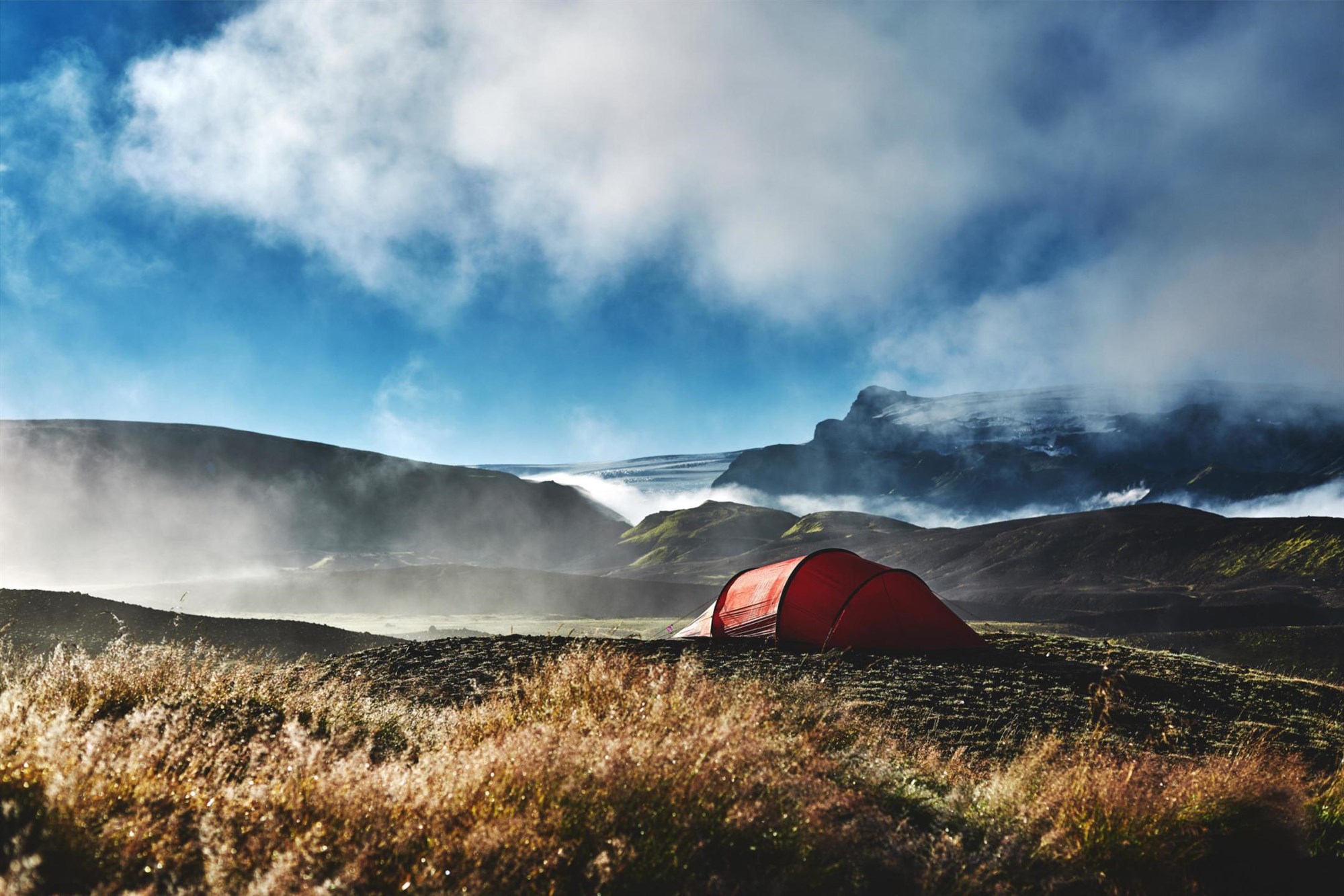 A bright red tent pitched in the Icelandic highlands near Langisjór, surrounded by dramatic fog, mossy hills and distant glaciers – a breathtaking view of Iceland’s wild nature.
