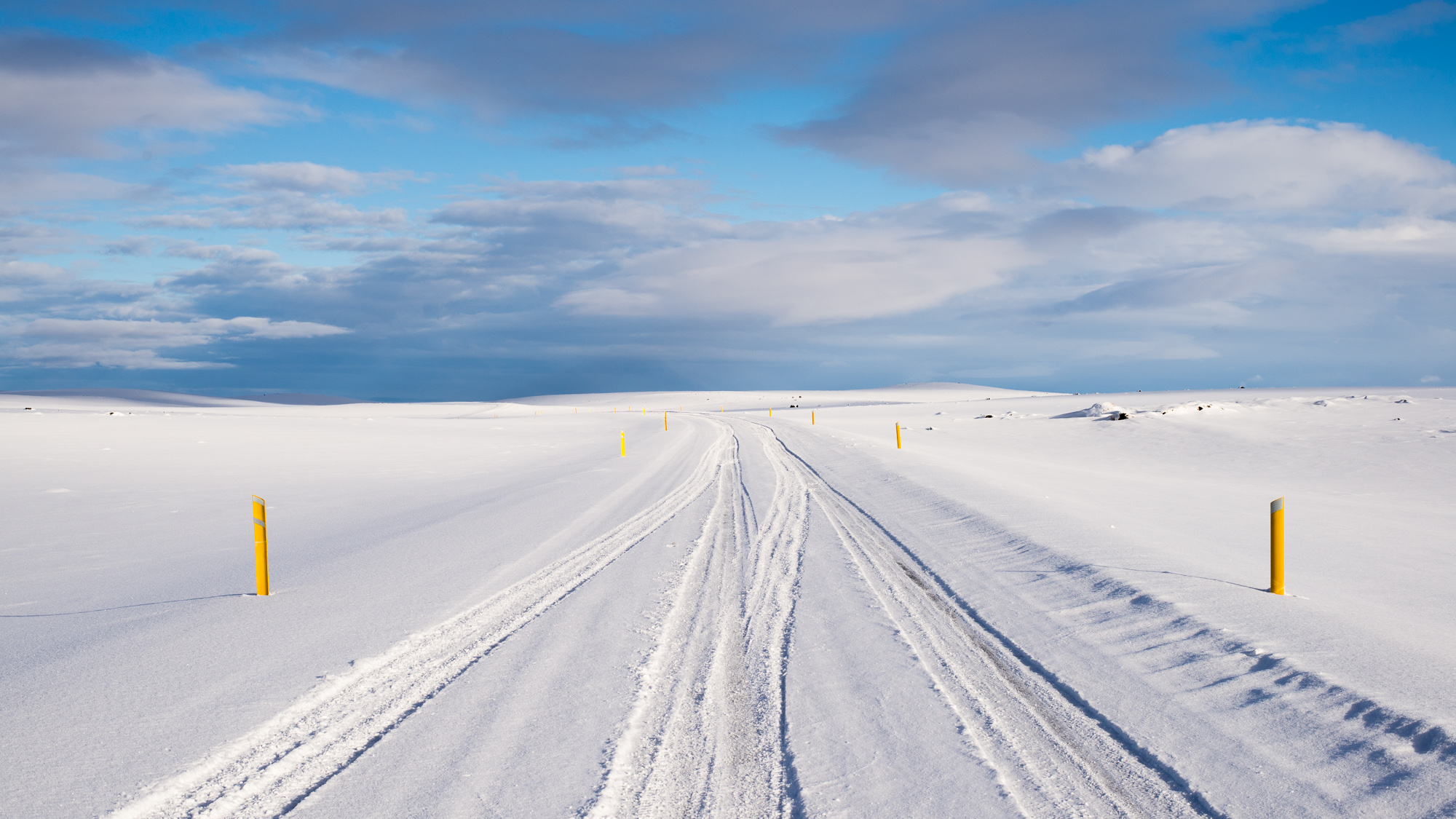 A vast stretch of snow-covered road in Iceland, completely blanketed in white, with no other signs of life, offering a quiet and isolated winter scene