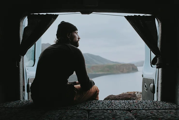 Traveler sitting inside a campervan in Iceland during a cold road trip morning surrounded by dramatic landscapes.