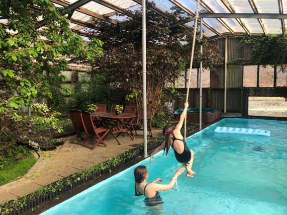 Poolside Fun at Heydalur Campsite Two kids playing by the rope swing in Heydalur’s indoor pool, surrounded by plants and soft light – the most photogenic dip in the Westfjords.