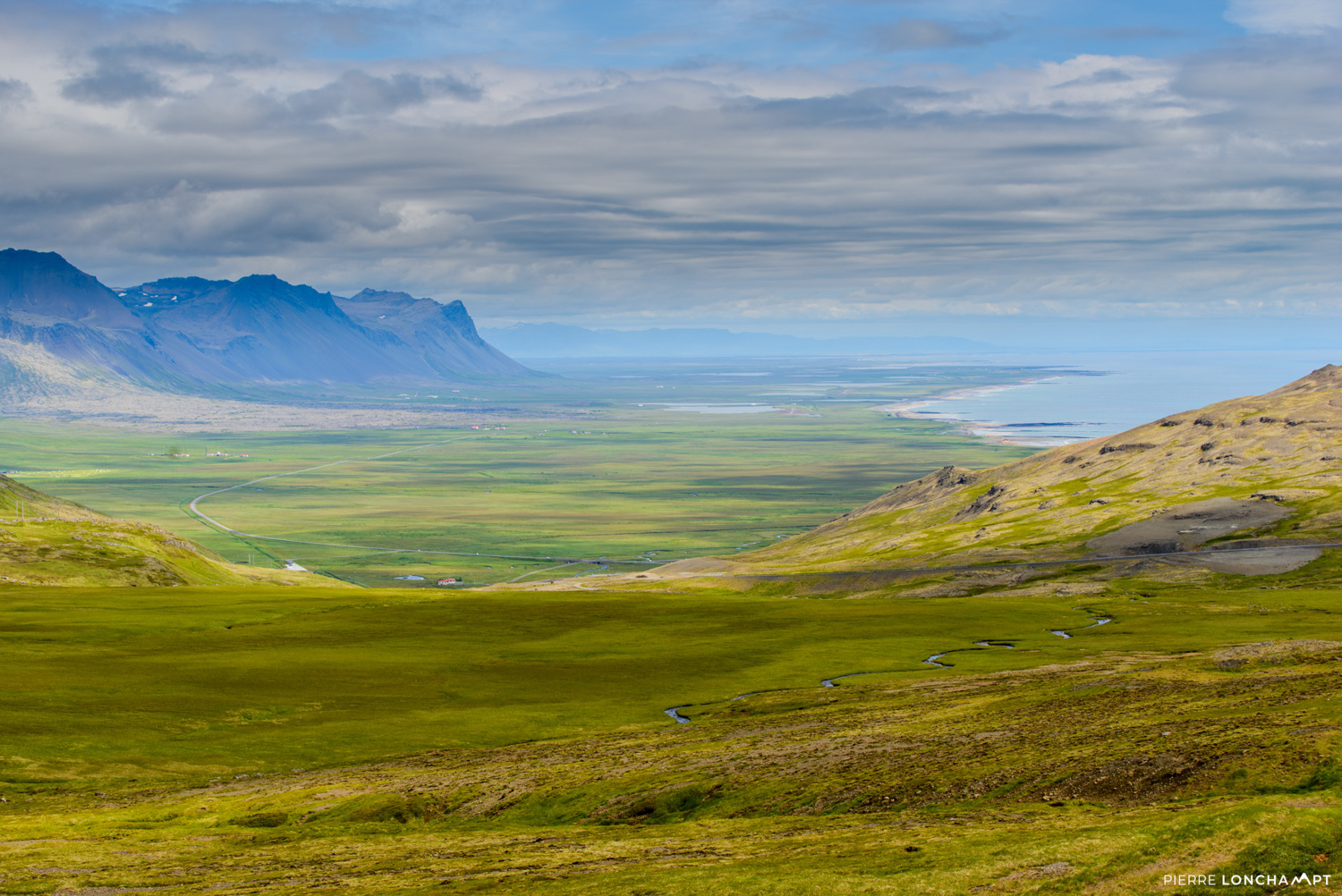 A serene Icelandic valley with rolling green fields and distant mountains, a perfect view during a campervan road trip in Iceland