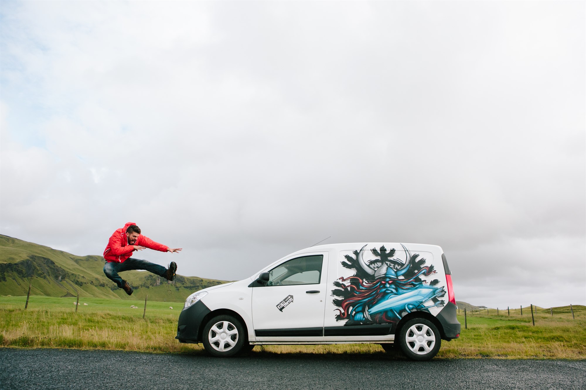 A close-up of a KuKu Campers van with signature graffiti artwork and a bold traveler jumping in front of it – the perfect symbol of KuKu’s wild and free campervan spirit in Iceland.