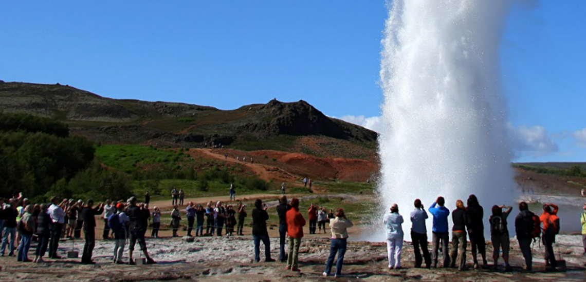 Tourists gather around Strokkur just before it erupts, capturing that perfect Iceland moment where excitement meets geothermal chaos.