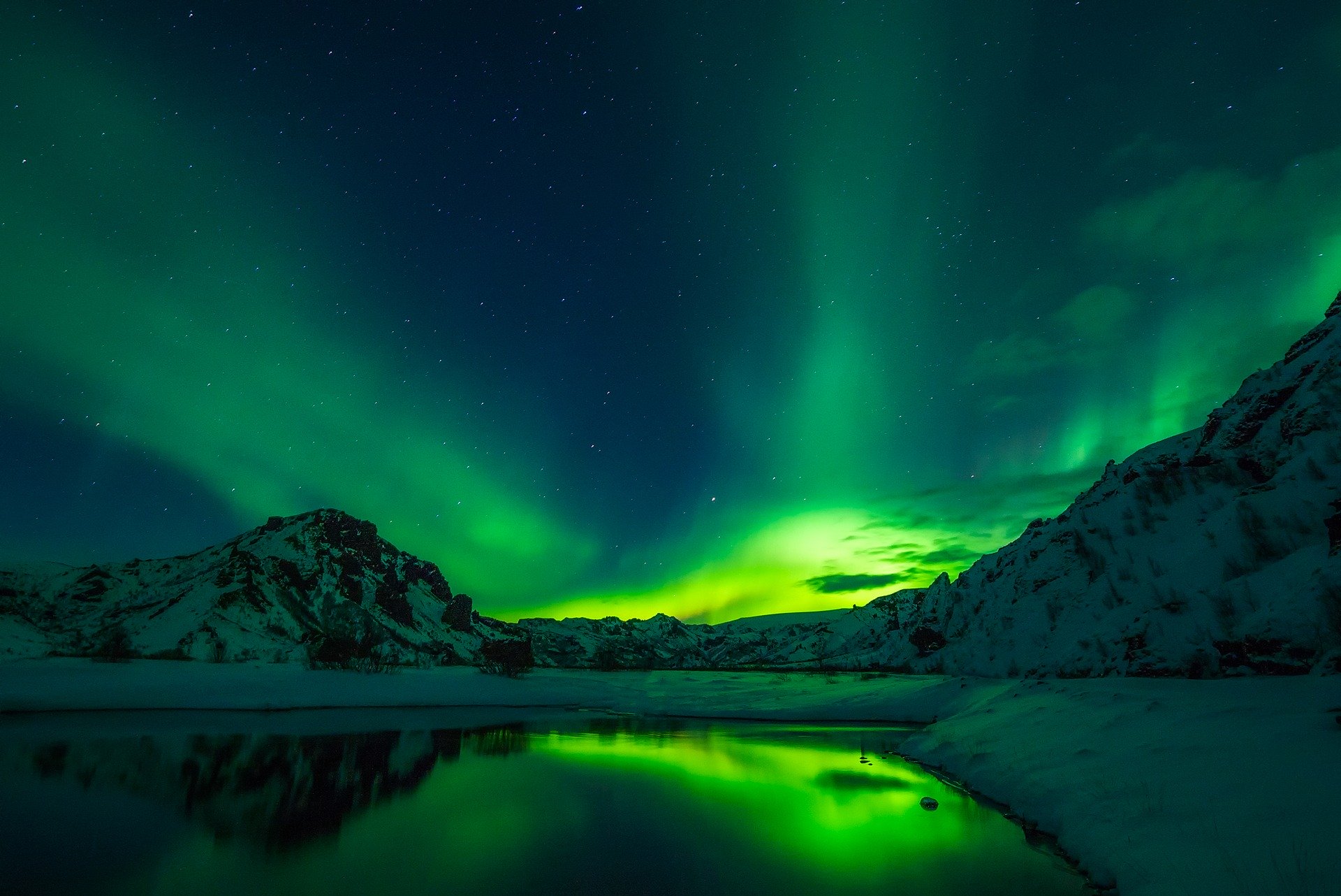 Aurora boreale verde in Islanda di notte, con un lago in primo piano e le montagne sullo sfondo.