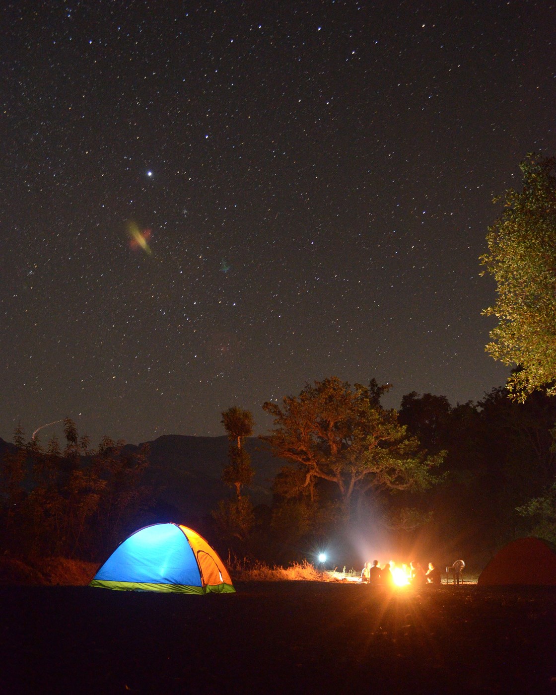 Camping tents with a crackling campfire in the foreground, as the night sky above Iceland is illuminated by countless stars, offering a peaceful and awe-inspiring moment in nature