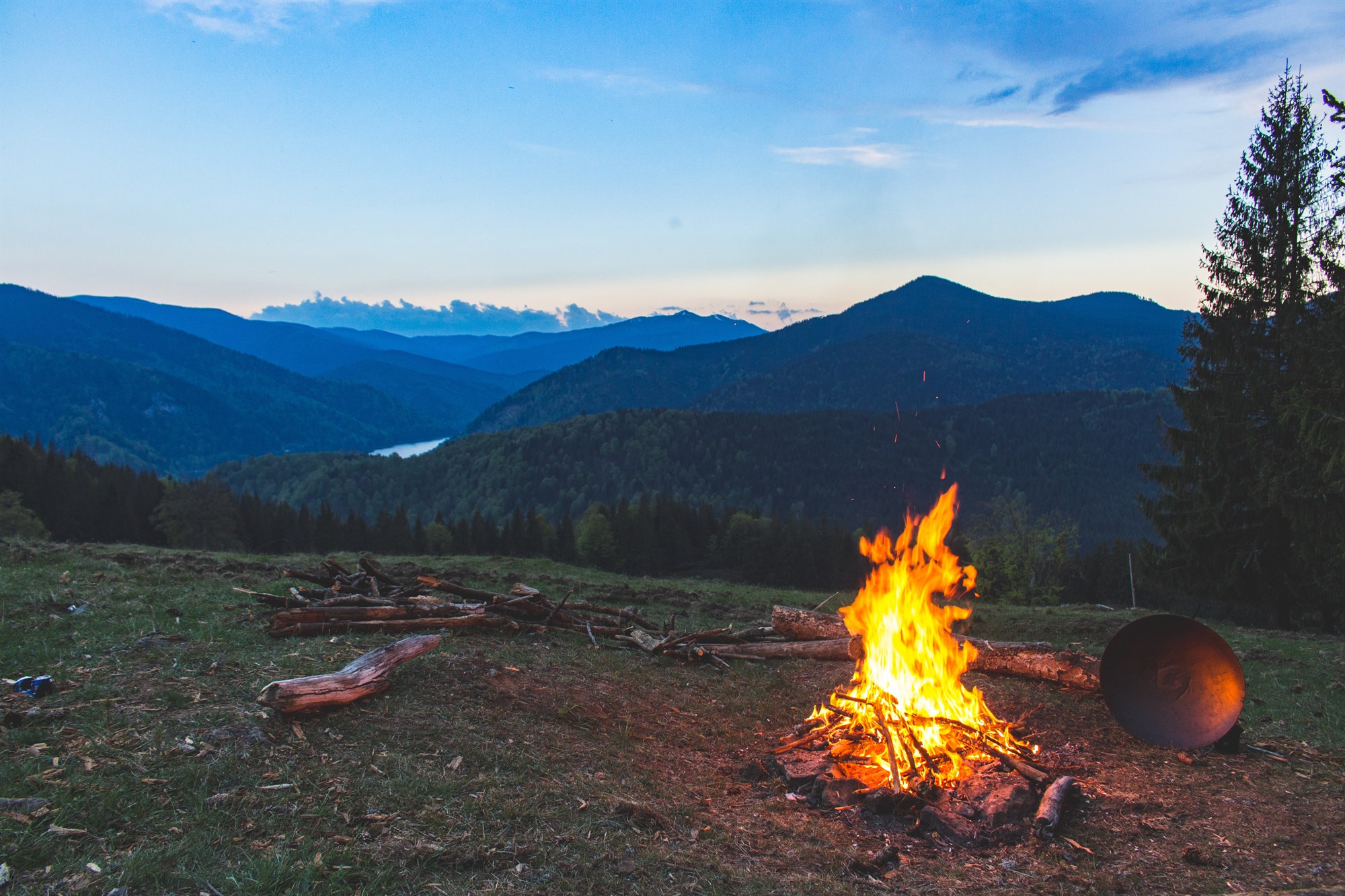 A warm campfire burning in the heart of an Icelandic forest, with majestic mountains towering in the background, creating a cozy and adventurous atmosphere amidst nature