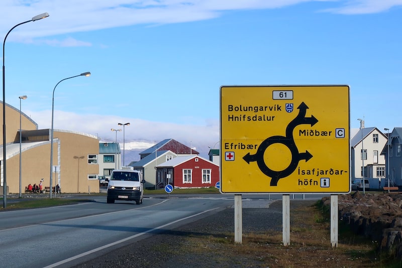 A yellow road sign in Iceland showing roundabout directions to different towns.
