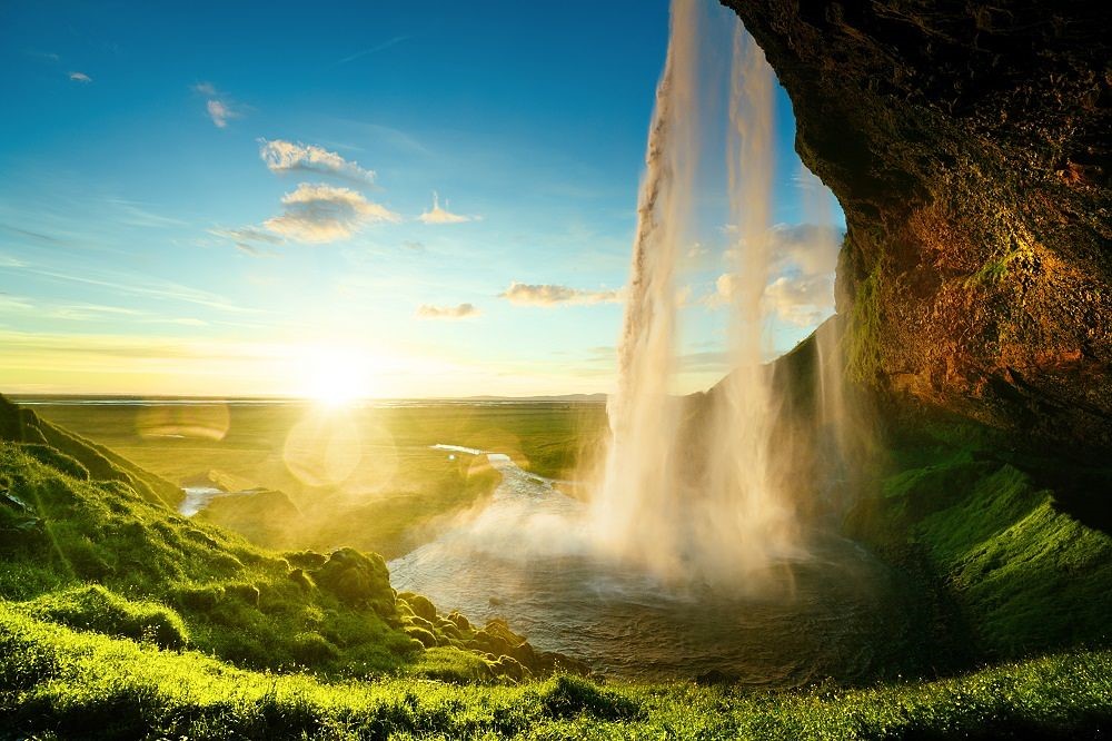 Cascata di Seljalandsfoss in Islanda con il sole, vista da dietro l'acqua che cade.