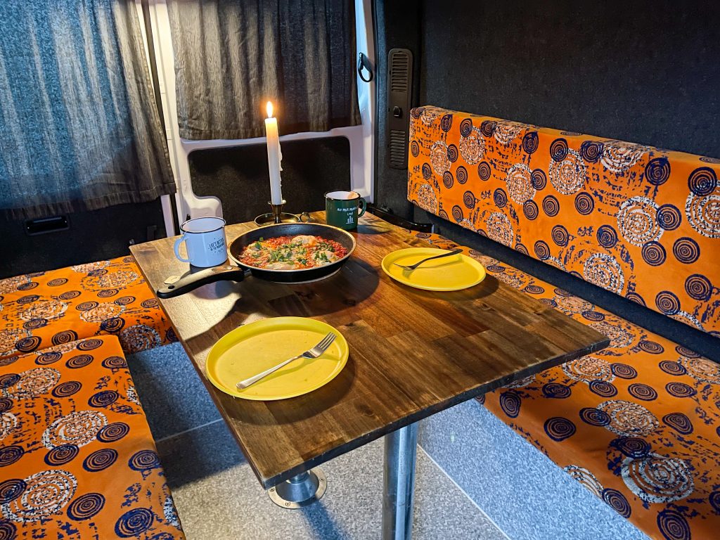 A cozy campervan dinner setup with a candlelit pan, colorful seats and that signature KuKu charm.