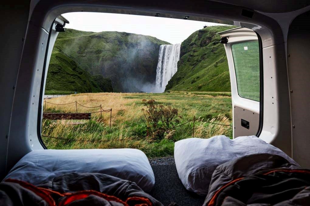 The view from inside a campervan parked near Skógafoss waterfall in Iceland, with pillows and sleeping bags ready for a night next to one of the country’s most iconic spots.