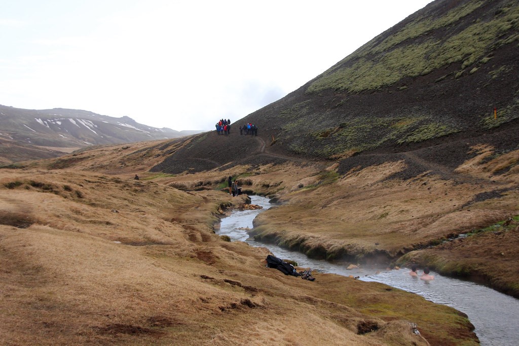 people bathing in the Reykjadalur hot river on the foreground and people hiking in the background 