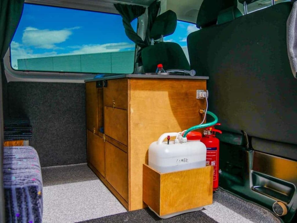 Inside a campervan showing water storage tank and sink system, useful for managing water during an Iceland trip.