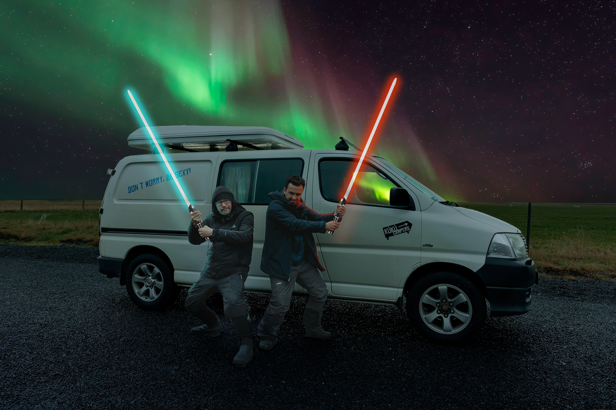Two KuKu Campers heroes battle it out with lightsabers next to their van while the aurora borealis lights up the Icelandic night sky.